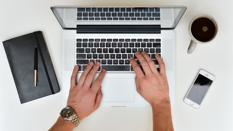 hands typing on a laptop with a journal to the side