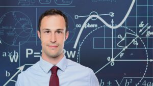 A man in a tie. Behind him are multiple statistical graphs and formulas