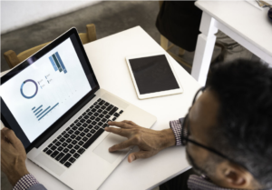 A man works on a laptop. Statistical graphs can be seen on his screen.