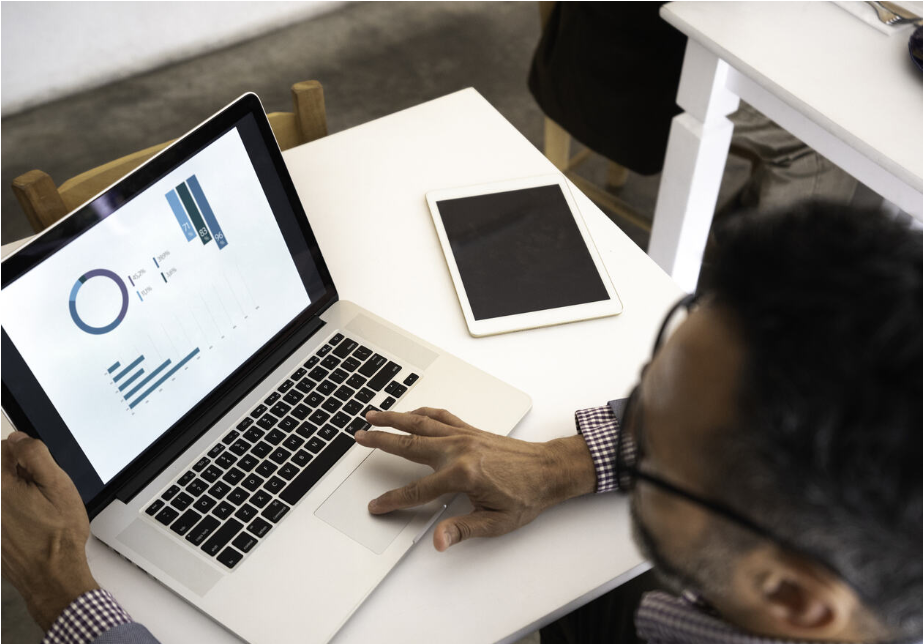 A man works on a laptop. Statistical graphs can be seen on his screen.