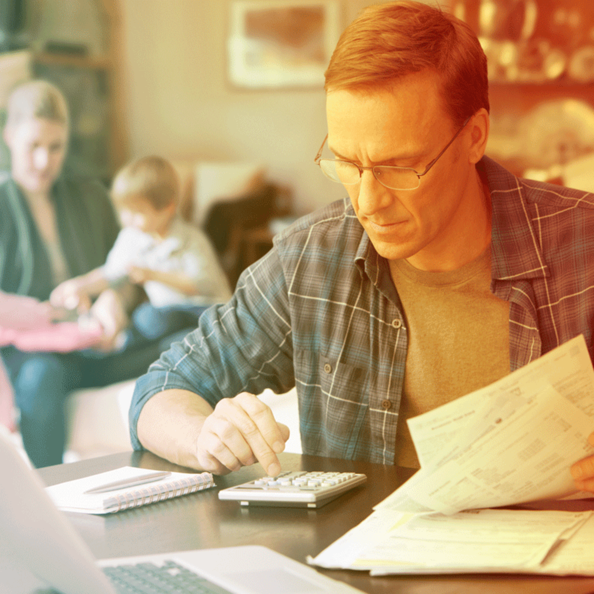 A father working on bills with a calculator. Behind him is a mother and child.
