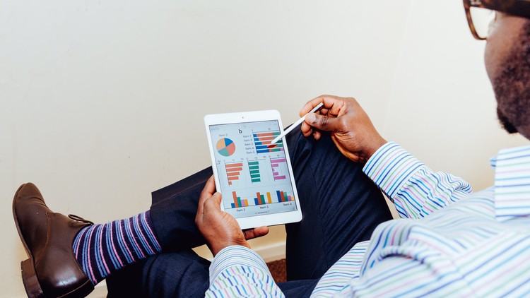 Looking over the shoulder of a man in business attire as he reads an ipad with financial graphs