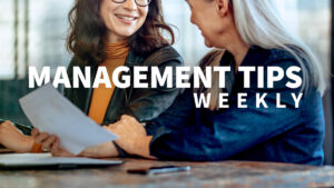 Two women looking at a document together. The words Management Tips Weekly are on the screen.