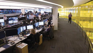 An open office corporate setting with many people at desks reviewing financial data