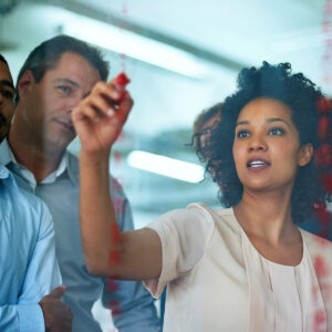 People in a business setting writing on a transparent board