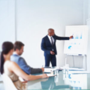 A person presenting to a boardroom with charts in the background.